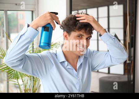 Handsome young man applying hair spray on his curly hair in hallway Stock Photo