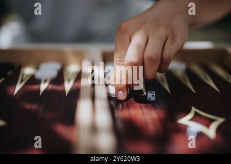 Close-up of hand rolling dice on a wooden backgammon board in a strategic and engaging game setting outdoors. Concept of leisure, concentration, and Stock Photo