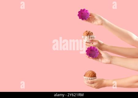 Female hands with baking forms and muffins on pink background Stock Photo