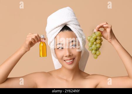 Happy young Asian woman with bottle of cosmetic grape seed oil on brown background Stock Photo