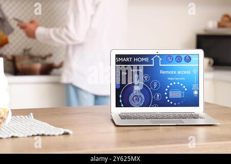 Laptop with smart home application on table against man using mobile phone in kitchen, closeup Stock Photo