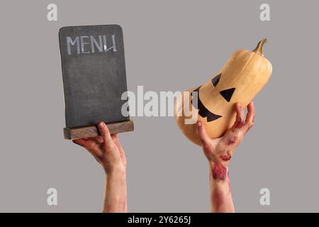 Zombie hands holding pumpkin and menu board on grey background. Halloween celebration Stock Photo