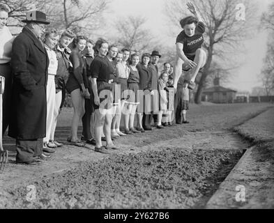 Busy under special training for the forthcoming Olympic Games, at the News of the World Sports Ground, Mitcham are girls from every walk of life, from bank clerks to housewives. They are under the watchful eye of Mrs M.Cornell, holder of the British women's long jump record, and official Olympic coach. Picture shows: watched by fellow club members long jumper Eileen Brewer takes leave of terra firma under the eyes of Mrs M.Cornell (dark jumper, foreground),  as she puts an Olympic training today at Mitcham.  Eileen is a housewife in 'private life'.  25  January 1948 Stock Photo