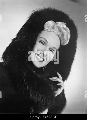 Champagne - blonde Adele Jergens smiling Columbia Pictures' star is ready for January snow in this plush silver fox fur. Peeping from under the luxurious hood Adele's blonde curls make a delicious contrast and a camera - worthy composition. 16 January 1948 Stock Photo