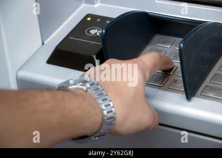 ATM machine and close-up man hand pushing on the pin button. Hand entering personal identification number on ATM dial panel Stock Photo