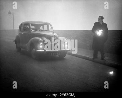 Traffic chaos in the fog London blacked out - A blanket of fog which covered London , brought road and rail traffic to a crawl and halted ships and planes .  Many passengers in public vehicles and private cars helped the drivers along on their journey by walking in front of the vehicles with lighted torches or lighted beacons .  Photo shows:  A pedestrian helps a motorist along by holding a lighted beacon to show him on his way , picture taken in the City of London today  6 December 1952 Stock Photo