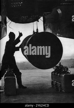 Seen in silhouette against the sky at 'bombing-up time' an RAF 'cookie' on the famous 4000 pounders - which have been dropped in hundreds on Berlin in the recent raids - rises slowly into position in the capacious bomb bay of a Lancaster.  Winches in the body of the bomber are hoisting the 'cookie' into its rack, on either side of which are incendiary containers, each holding more than a hundred fire-bombs.  The armourer's 'thumbs up' signal shows that everything is proceeding to his satisfaction.  The load seen here is only a party of the bomb capacity of any Lancaster, which normally carries Stock Photo