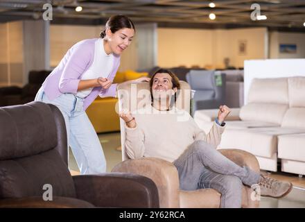 Guy and girl sitting in armchairs and deciding on buying in furniture section Stock Photo