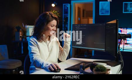 Joyous woman doing software quality assurance celebrating after reading source code and finding no errors. Cheerful engineer excited after inspecting coding on desktop PC, seeing no issues, camera B Stock Photo