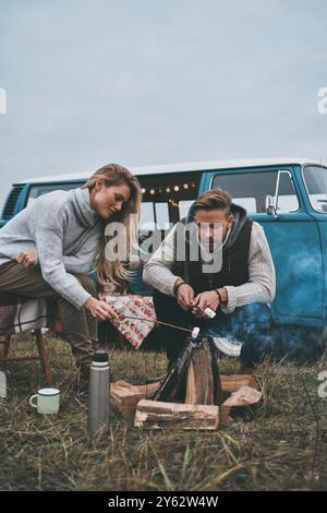 Looks delicious.  Beautiful young couple roasting marshmallows over a campfire while enjoying their road travel Stock Photo