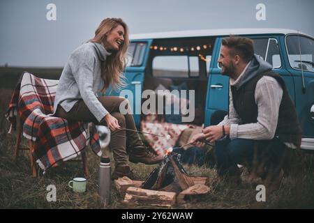 Leave all your worries behind.  Beautiful young couple roasting marshmallows over a campfire while enjoying their road travel Stock Photo