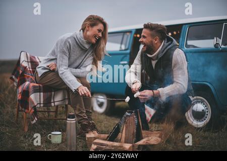 Perfect place to stay.  Beautiful young couple roasting marshmallows over a campfire while enjoying their road travel Stock Photo