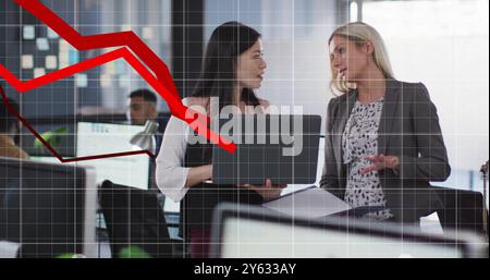 Discussing business strategy, two women with laptop over declining financial graph image Stock Photo