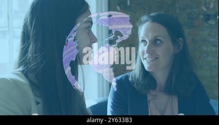 Digital globe image over two businesswomen having conversation in office Stock Photo