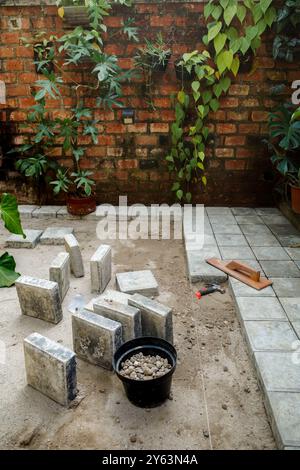 Concrete block floor construction work for courtyard patio as house exterior with green hanging garden on brick wall in the background Stock Photo