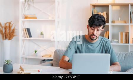 Online job. Remote freelance. Software development. Smart computer engineer guy working from home office using laptop at modern workplace interior with copy space. Stock Photo