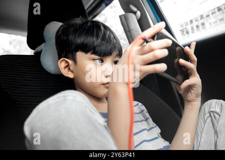 An Asian boy enjoying playing online game on smartphone inside a car Stock Photo
