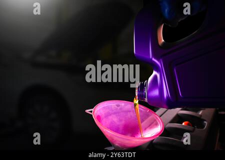 Engine oil is poured into the funnel by car mechanic for lubricating the engine , copy space for text and car repair blurred on background , Car maint Stock Photo