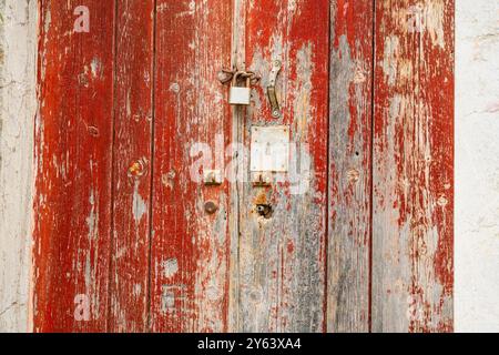 Rustic, flaking, peeling red paint on a rotting and decaying door with rusty lock and keyhole at an abandoned house’s doorway Stock Photo