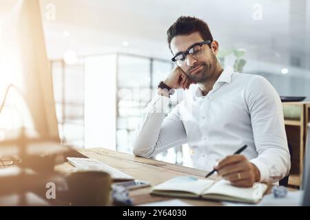 Bored, businessman and writing with book for schedule, planning or business report at office. Young, tired man or lazy employee taking notes for Stock Photo