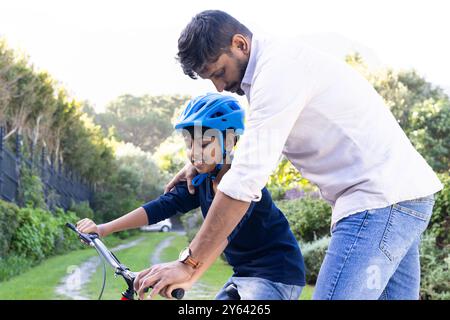 indian father teaching young son to ride bicycle, bonding outdoors in nature Stock Photo