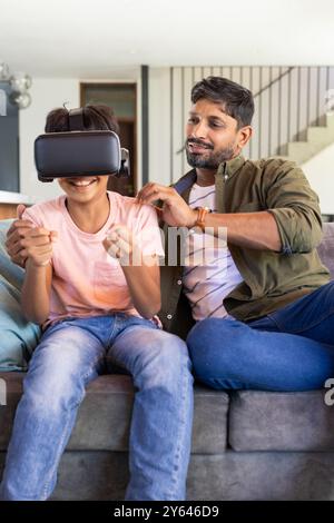 indian father watching son using VR headset while sitting on couch at home Stock Photo