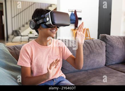 Using VR headset, Indian boy sitting on couch and playing virtual reality game Stock Photo