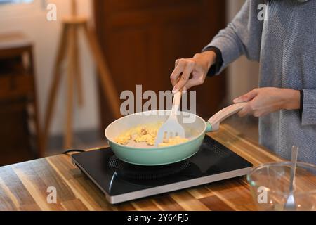 Happy young asian woman preparing scrambled eggs in the kitchen Stock Photo