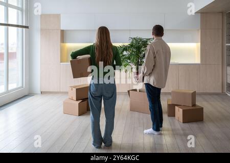 New home owners with boxes and houseplant in hands. Housewarming relocation in mortgage apartment. Stock Photo