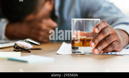 Drunk black employee sleeping at workplace, holding glass with alcohol Stock Photo