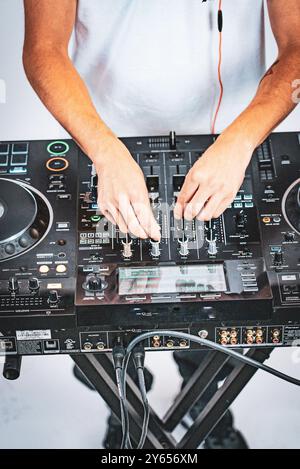 DJ mixing music on a professional sound mixer with hands adjusting knobs and sliders. Stock Photo