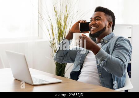 Black businessman having coffee break and taking on phone in office Stock Photo