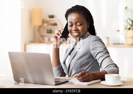Afro Businesswoman Taking Notes While Having Phone Conversation In Modern Office Stock Photo