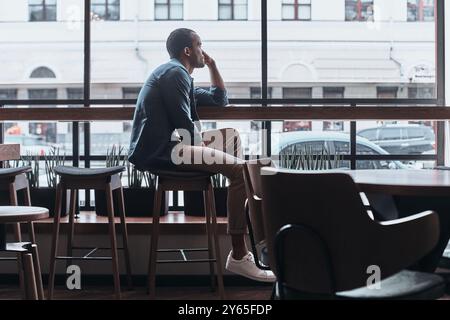 Enjoying nice day. Thoughtful young man looking outside while sitting in the cafeteria Stock Photo