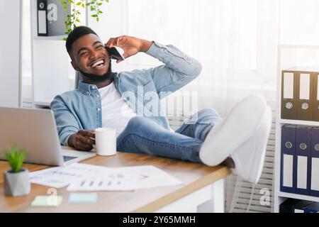 Joyful black manager talking on phone while having break at work Stock Photo