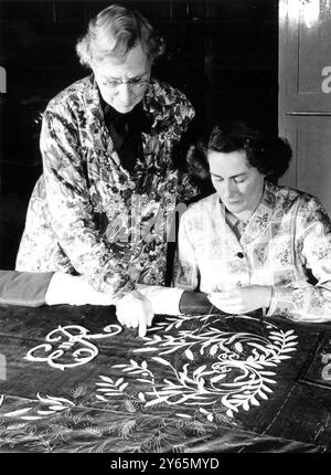 At the Royal School of Needlework in London ,  Queen Elizabeth II 's 18 feet long Coronation Robe lies on an embroidery table while skilled needleworkers embroider it with gold thread .  The Royal Cypher 'E.R.' has been completed on one side and the design of olives and wheatsheafs to denote peace and prosperity is in the process of being woven into the fabric in gold .  In this picture Miss M Bartlett works on the olives and wheatsheafs design , which is the bckground motif to the Royal Cypher and Crown .   11th February 1953 Stock Photo