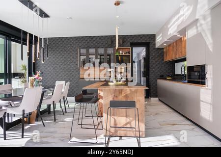 Luxurious modern kitchen features elegant seating, a stylish wooden island, designer light fixtures, and integrated appliances, set in an open airy sp Stock Photo