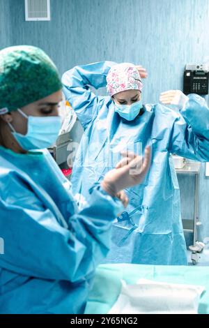 Two surgeons in scrubs and masks preparing for a procedure in a hospital operating room, focusing on their tasks amid sterile medical equipment Stock Photo