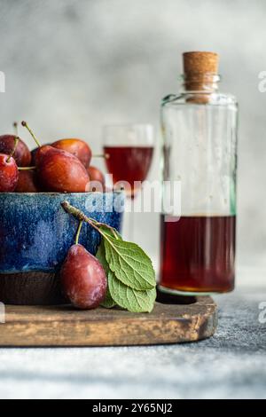 A bowl of fresh, organic plums alongside a bottle of homemade plum liqueur, captured from the side. The image highlights ripe plums with vibrant color Stock Photo