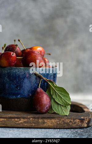 Freshly harvested organic plums, displayed in a rustic blue bowl, accented with a vibrant green leaf on a wooden surface. Ideal for natural food prese Stock Photo