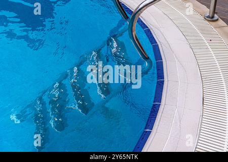 High-angle view of a tranquil swimming pool with shimmering blue waters, featuring a sleek metal ladder and curved mosaic-tiled edges, perfect for sum Stock Photo