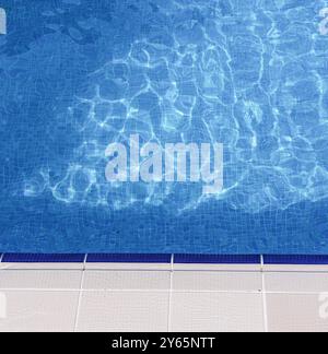 A vibrant close-up view of a swimming pool, highlighting the clear blue water and textured tiles at the water’s edge Stock Photo