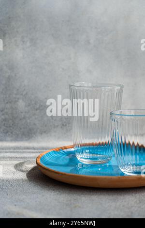 Two empty ribbed glasses rest on a blue ceramic plate, illuminated by natural light The simple and elegant composition highlights the textures and tra Stock Photo