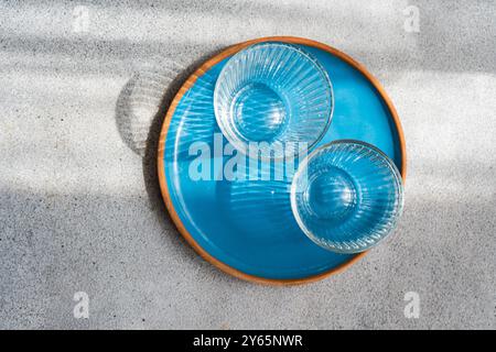 An artistic image showing two transparent blue glass bowls arranged inside a larger blue bowl, all set on a sandy surface Stock Photo