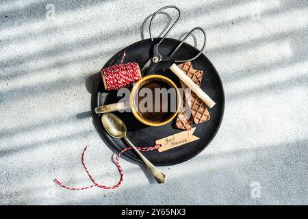 Top view of a cozy morning coffee scene featuring a black tray with a cup of coffee, scissors, wafers, chocolate, vintage spoons, and a Good Morning n Stock Photo