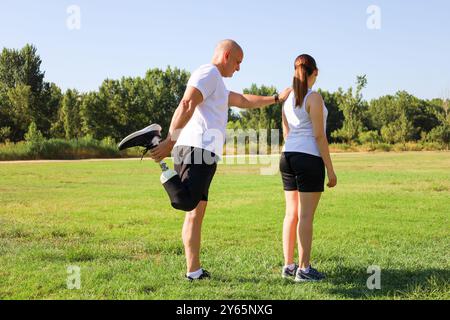 A man with an amputated leg using a prosthetic limb is seen bonding with his young daughter in a sunlit park, both dressed in athletic wear Stock Photo