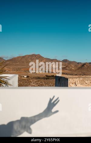 Cropped unrecognizable shadow of a hand projected on a white wall, framing the scenic mountains and plains of Cabo de Gata in Almeria, Spain. Stock Photo