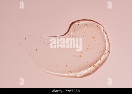 High-quality image showcasing the smooth texture and shiny gold specks of a 24k gold cream gel smeared on a pink background. Stock Photo