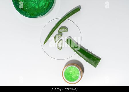 Overhead view of fresh aloe vera leaves, sliced pieces, and a jar of bright green aloe gel arranged neatly on a pure white background, emphasizing cle Stock Photo