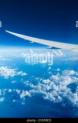 Captivating aerial view of the serene blue sky and fluffy clouds as seen from an airplane window, showcasing the wing tip. Stock Photo